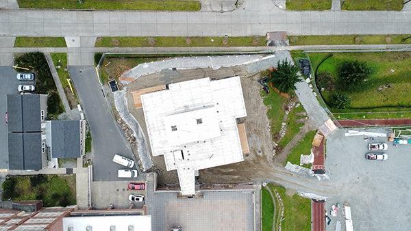 aerial view directly over 在建的建筑物 showing a narrow connection to the existing building, 在图像的顶部有一条路, 左边有个停车场